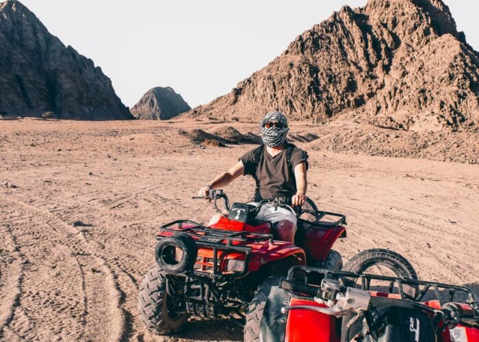 man riding red atv man riding red atv on brown sand during daytime